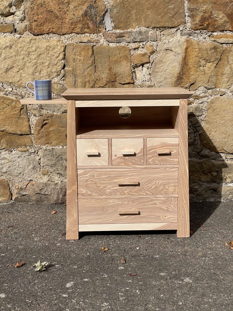 "Chaffinch" bedside cabinet made by Iain Stirling of Chapelhill Fine Furniture. Front view with mug on tray.