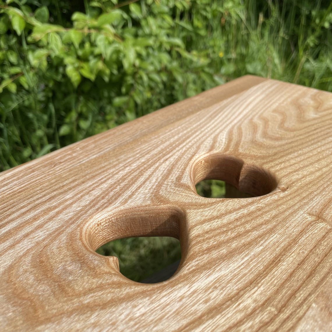 Scottish creepie stool made from Scottish elm with a double-heart pair of finger holes in the top surface, made by Chapelhill Fine Furniture.