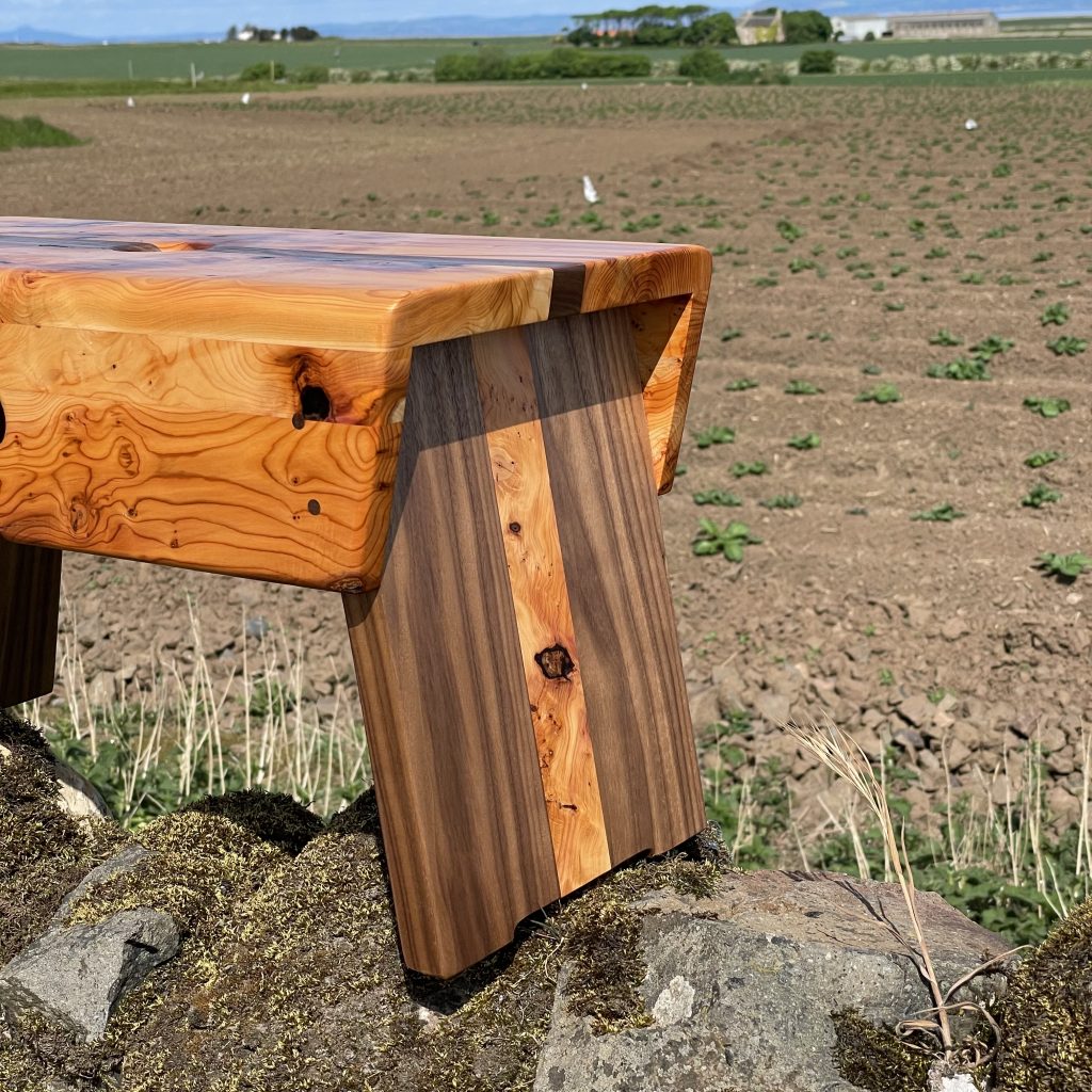 Yew and walnut Scottish creepie stool made by Chapelhill Fine Furniture in Scotland, with Tantallon Castle and Bass Rock in background.