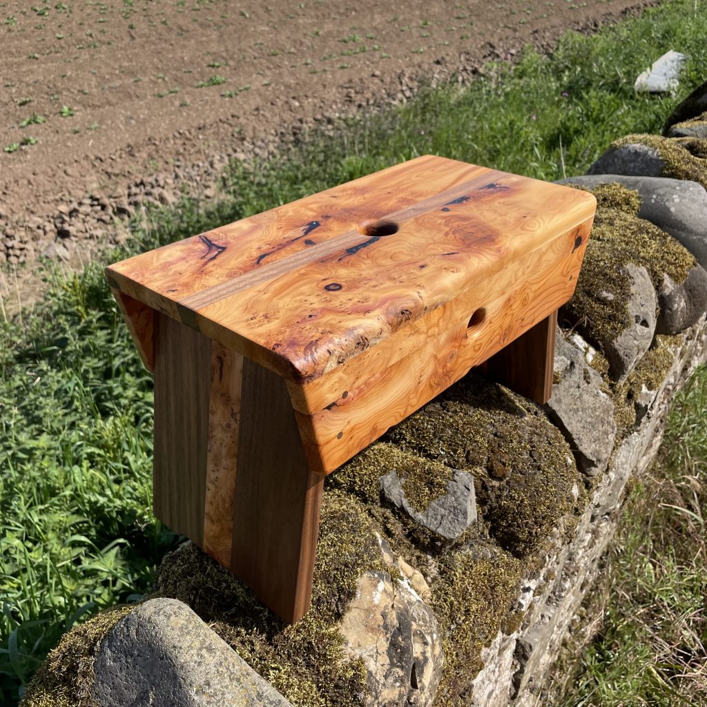 Yew and walnut Scottish creepie stool made by Chapelhill Fine Furniture in Scotland, with Tantallon Castle and Bass Rock in background.
